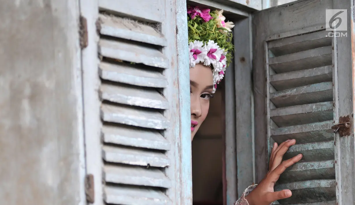 Seorang gadis mengintip dari jendela rumah saat hendak mengikuti upacara adat Ngarot di Desa Lelea, Indramayu, Jawa Barat, Rabu (19/12). Para gadis dihias dengan berbagai jenis bunga warna-warni yang dianggap simbol kesuburan. (Merdeka.com/Iqbal Nugroho)