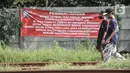 Warga melintas di depan spanduk pemberitahuan terkait rencana penggusuran dekat Jakarta International Stadium, Kelurahan Papanggo, Tanjung Priok, Jakarta Utara, Selasa (22/2/2022). (merdeka.com/Iqbal S. Nugroho)