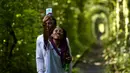 Pasangan berselfie di sepanjang bekas rel kereta api atau 'Tunnel of Love' dekat desa Ukraina Klevan, Rivno, (6/8). Seorang turis mengatakan jika melewati terowangan ini keinginan untuk jatuh cinta akan menjadi kenyataan. (AFP Photo/Sergei Supinsky)