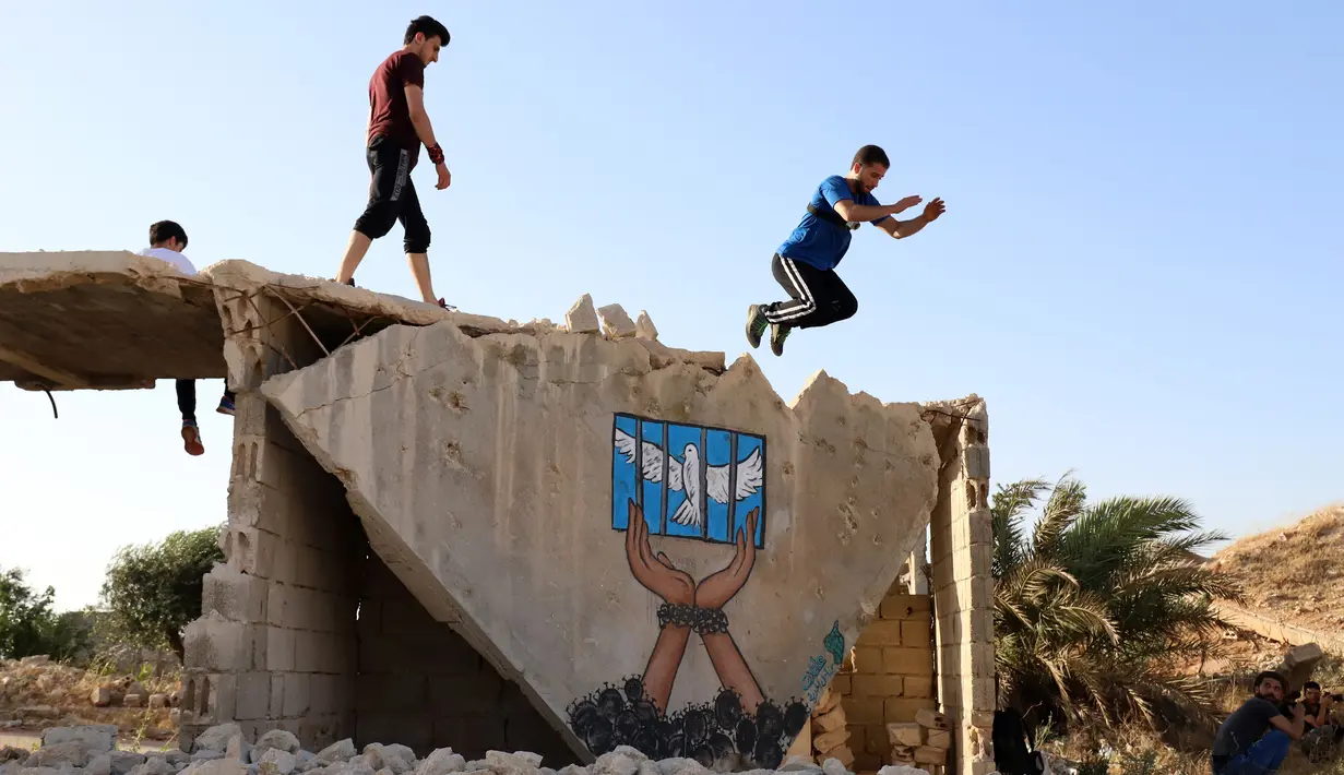 Pemuda Suriah melakukan olahraga ekstrem parkour di atas reruntuhan bangunan yang hancur akibat serangan pasukan rezim di kota Binnish di provinsi barat laut Idlib pada 17 Juni 2020. Parkour merupakan olahraga ketangkasan yang terdiri dari lari, melompat, salto dan berayun. (Abdulaziz KETAZ / AFP)