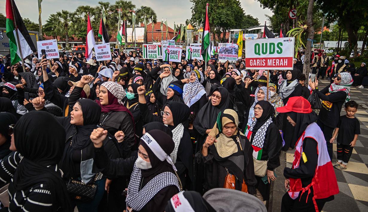 Peringatan Hari Al-Quds Internasional dicetus oleh Ayatollah Khomeini pada 1979, momen ini melibatkan aksi pawai damai di berbagai negara, termasuk Indonesia. Tampak dalam foto, orang-orang memegang plakat dan bendera Palestina selama aksi unjuk rasa memperingati Hari Al-Quds, di Surabaya, Jawa Timur, Jumat (13/3/2026). (Juni KRISWANTO/AFP)