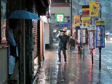 Seorang pejalan kaki menutupi kepalanya dengan tas di samping salah satu halte bus kawasan Quarry Bay, Hong Kong, pada 5 Agustus 2025, di tengah peringatan hujan badai hitam yang dikeluarkan oleh observatorium cuaca kota. (Tommy WANG/AFP)