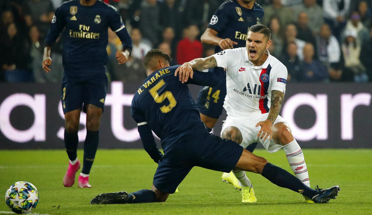 Striker Paris Saint-Germain, Mauro Icardi, terjatuh saat berebut bola dengan bek Real Madrid, Raphael Varane pada laga Liga Champions di Stadion Parc des Princes, Rabu (18/9/2019). PSG menang 3-0 atas Real Madrid. (AP/Francois Mori)