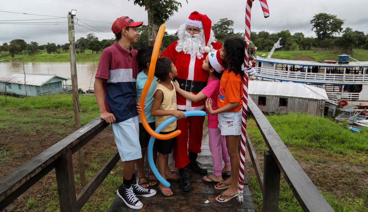 Relawan Jorge Alberto Barrozo, yang mengenakan kostum Sinterklas, berbicara dengan anak-anak saat tiba untuk mengantarkan hadiah di komunitas tepi sungai di daerah pedesaan Careiro da Varzea, negara bagian Amazonas, Brasil pada Sabtu 20 Desember 2025. (Michael DANTAS/AFP)