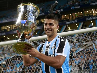 Pemain Gremio, Luis Suarez mengangkat trofi setelah memenangkan Gaucho Championship di Arena do Gremio Stadium, Porto Alegre, Brasil, 8 April 2023. Suarez menjadi pencetak gol penentu kemenangan ke gawang Caxias pada laga leg kedua final. (AFP/Silvio Avila)