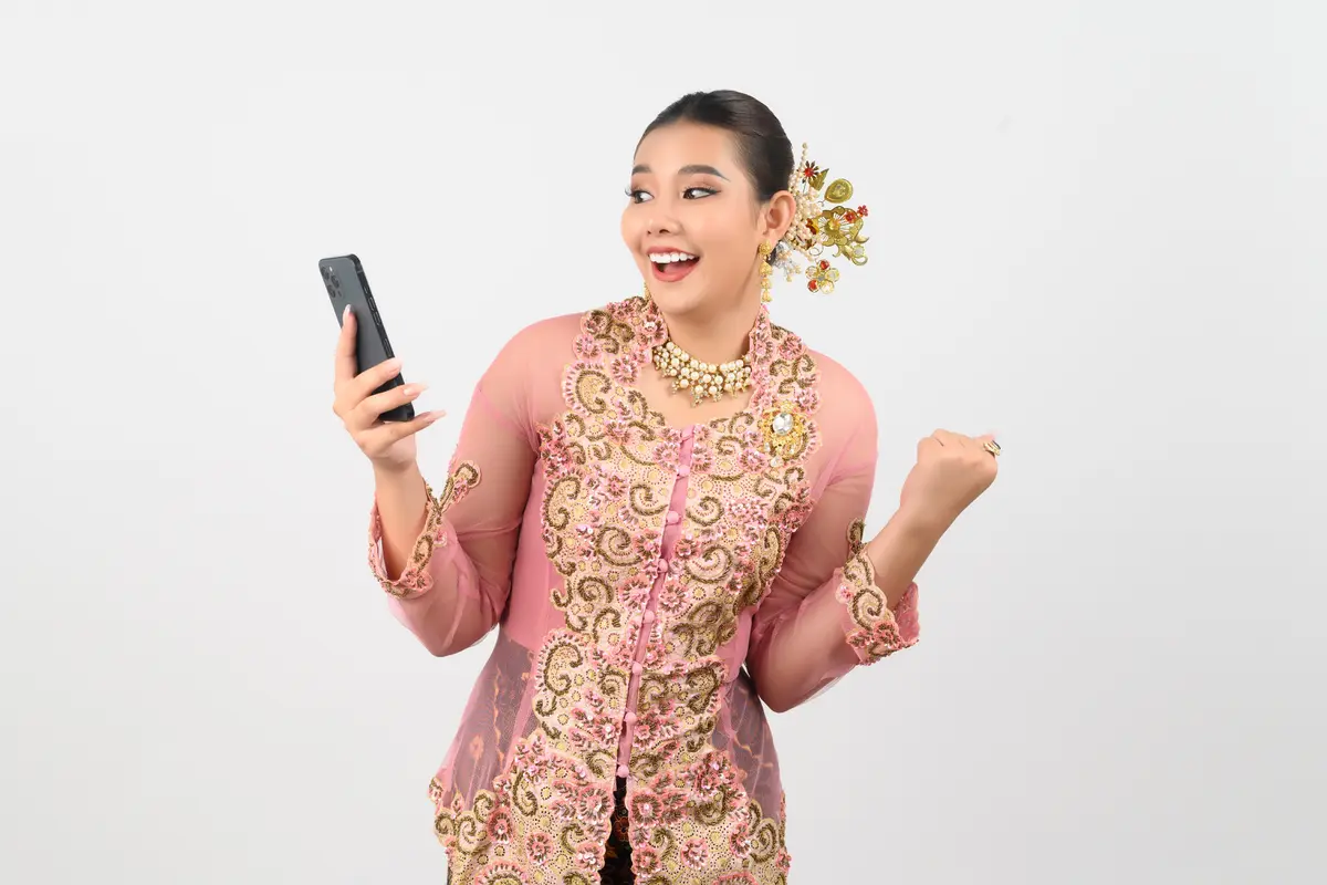 Seorang perempuan mengenakan kebaya sambil memegang HP (Foto Dok: Freepik/johnstocker)