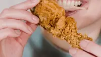 Seorang wanita sedang menggigit ayam kentucky. (Liputan6.com/Pexels/Tim Samuel)
