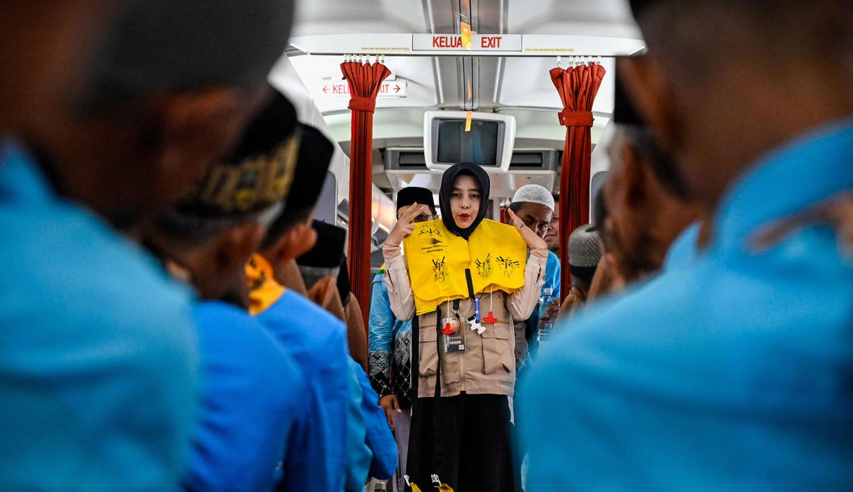 Awak kabin memeragakan cara menggunakan jaket penyelamat kepada calon jemaah haji Indonesia di dalam pesawat Boeing 717 yang sudah tidak digunakan lagi selama sesi pelatihan keselamatan pra-keberangkatan di pusat embarkasi haji Banda Aceh pada Kamis 14 Mei 2026. (CHAIDEER MAHYUDDIN/AFP)