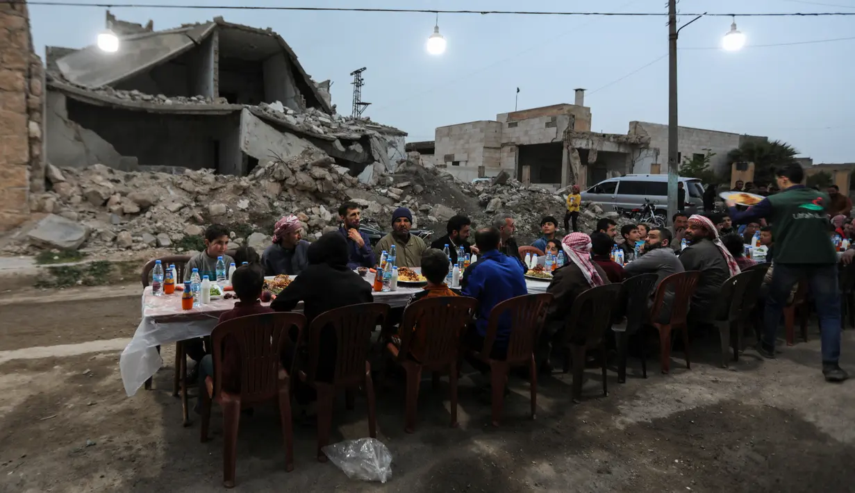 Warga Suriah berkumpul di daerah yang rusak berat untuk berbuka puasa di Tadef, dekat kota perbatasan al-Bab, yang dikendalikan pemberontak yang didukung Turki di Suriah (18/4/2022). Buka puasa ini diselenggarakan oleh sebuah LSM berkoordinasi dengan berbagai faksi lokal. (AFP/Bakr Alkasem)