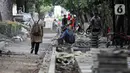 Pejalan kaki melintas saat pekerja menyelesaikan proyek revitalisasi pedestrian di kawasan Jalan Pattimura, Jakarta, Rabu (8/6/2022). Dinas Bina Marga DKI Jakarta merevitalisasi pedestrian dengan memperlebar menjadi tiga meter sehingga cukup luas untuk memberikan kenyamanan para pejalan kaki. (Liputan6.com/Faizal Fanani)
