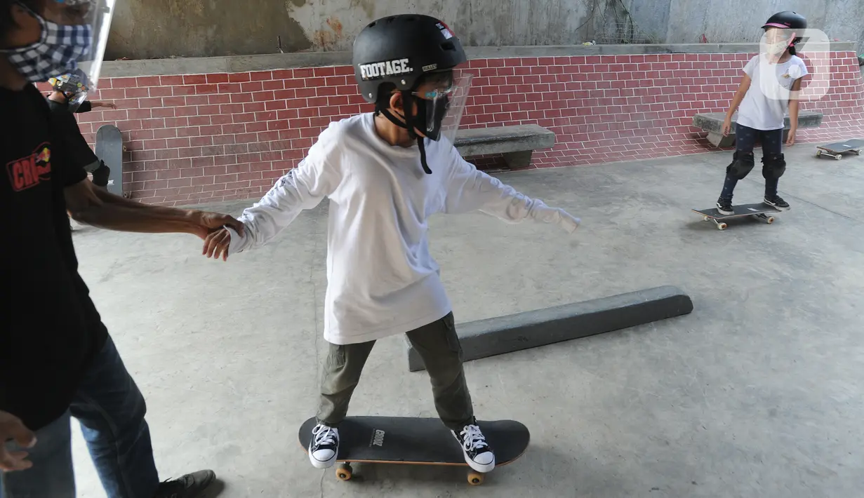 Instruktur melatih seorang anak menggunakan skateboard dengan memakai masker dan face shield di Crooz Shophouse di kawasan Duren Tiga, Jakarta Selatan, Minggu (2/8/2020). Mereka kembali melakukan latihan seminggu dua kali dengan menerapkan protokol kesehatan. (merdeka.com/Arie Basuki)