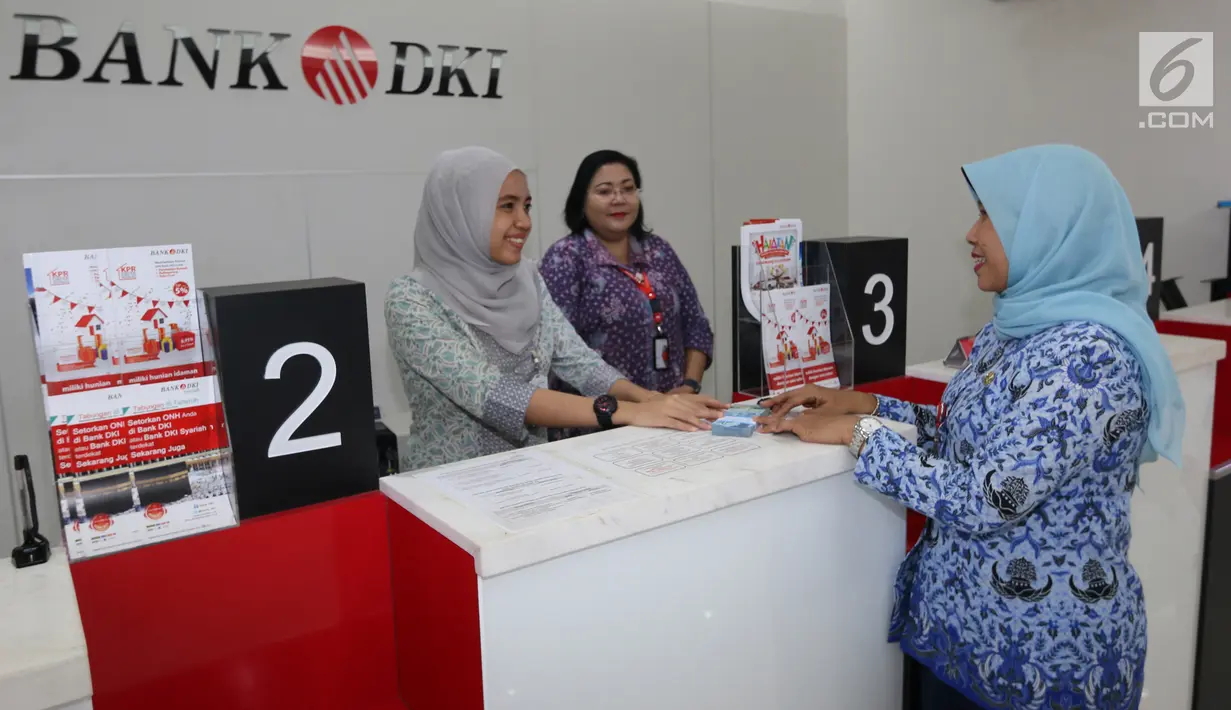  A customer wearing a blue headscarf is being served by a bank teller at a counter in a Bank DKI.