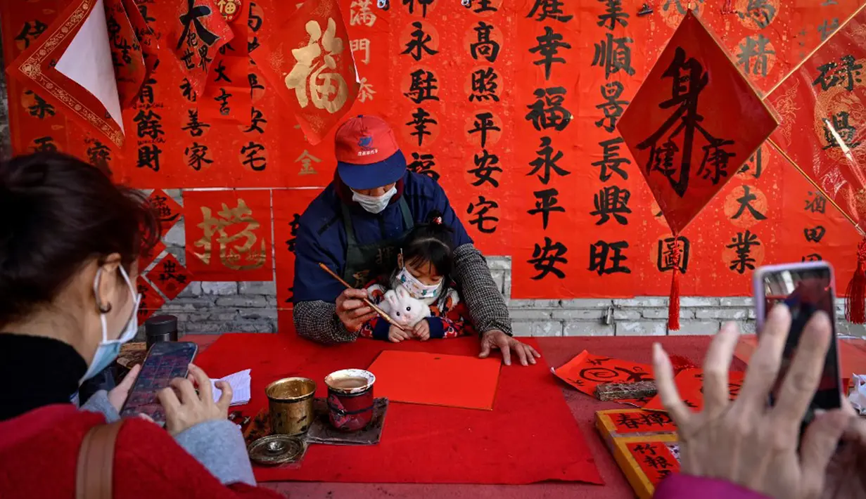 Seorang kaligrafer menulis kuplet musim semi, semacam dekorasi Tahun Baru Imlek, jelang dimulainya Tahun Baru Imlek di sebuah kios di Foshan, Provinsi Guangdong, China, 18 Januari. Kuplet adalah karya kaligrafi ala China dengan tinta hitam di atas kertas merah yang terdiri dari dua bait harapan atau pernyataan baik untuk menyambut Imlek. (Giok Gao/AFP)