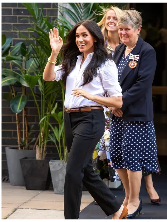 Gaya chic Meghan Markle dalam balutan kemeja lengan panjang yang digulung berwarna putih polos, dipadukannya mengenakan celana panjang hitam, belt cokelat dan heels cokelat yang serasi. [Foto: Instagram/sussexroyal]