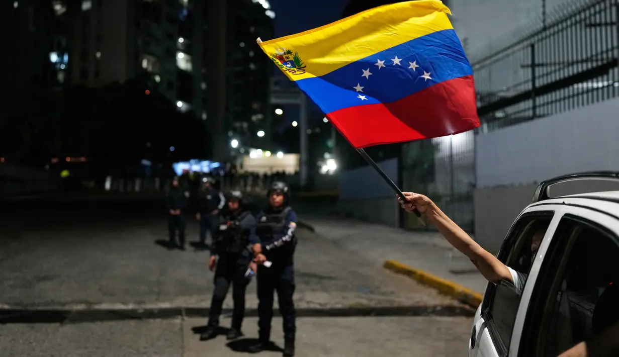 Percepatan pembebasan tahanan ini terjadi setelah penangkapan mantan Presiden Nicolas Maduro oleh militer Amerika Serikat pada 3 Januari 2026 lalu. Tampak dalam foto, Seorang pendukung oposisi mengibarkan bendera Venezuela dari sebuah kendaraan yang lewat di dekat El Helicoide, markas besar dinas intelijen dan pusat penahanan, setelah beberapa tahanan politik dibebaskan dari tahanan, Caracas, Venezuela, Minggu 8 Februari 2026. (AP Photo/Ariana Cubillos)