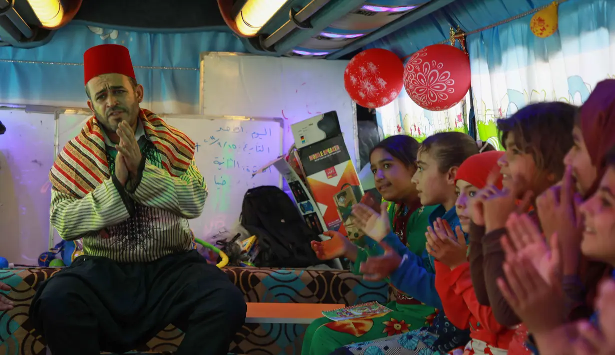 Anak-anak Suriah yang terlantar bernyanyi di sebuah bus yang diubah menjadi ruang kelas di dekat desa Hazano di Suriah barat laut (15/9/2019). Sejak proyek itu diluncurkan pada Mei, sekitar 1.000 anak telah mendapat manfaat dari program kelas bus ini. (AFP Photo/Aaref Watad)