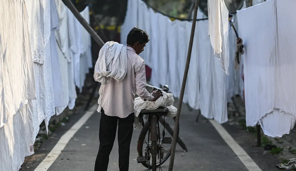 Seorang pekerja meletakkan pakaian yang sudah dicuci untuk dikeringkan di binatu terbuka, yang secara lokal disebut 'Dhobi Ghat' di New Delhi, India pada 14 Maret 2022. Dhobi Ghat adalah tempat yang menyediakan layanan cuci dengan cara tradisional. (Money SHARMA / AFP)