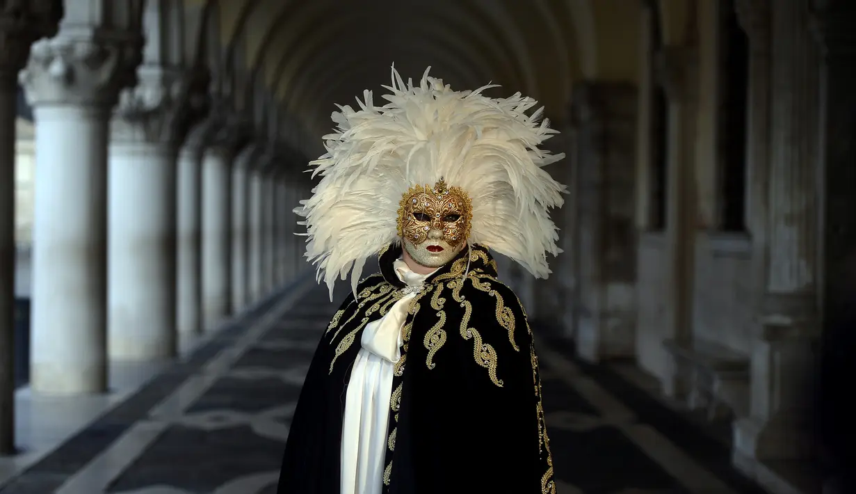 Seorang peserta bertopeng emas dan kostum tradisional berdiri di St Mark Square selama Karnaval Venesia di Italia, Sabtu (28/1). Karnaval ini bertema "Creatum: Civitas Ludens". (FILIPPO MONTEFORTE/AFP)