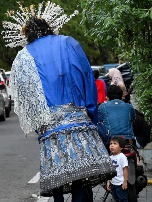 Foto pada 20 Maret 2019, bocah melihat ondel-ondel yang dioperasikan oleh seorang anak untuk mengamen di jalanan Jakarta. Seiring berjalan waktu, ondel-ondel yang dahulu sebagai ikon kesenian Betawi kini mudah ditemui di sejumlah jalan dan gang-gang di antara permukiman warga. (GOH CHAI HIN / AFP)