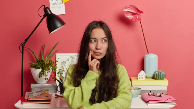 Seorang perempuan berambut panjang sedang berpikir dengan memegang pipinya menggunakan telunjuk (Foto Dok: Freepik/wayhomestudio)