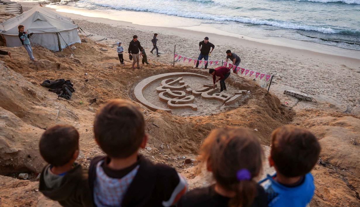 Karya seni tersebut merupakan bentuk ketahanan dan upaya untuk memberikan kegembiraan bagi warga Palestina yang terpaksa mengungsi akibat perang berkepanjangan antara Israel dan Hamas. Tampak dalam foto, anak-anak berdiri di atas bukit pasir di atas patung pasir dengan pesan ucapan "Selamat Datang, Ramadan" yang dibuat oleh seniman Palestina, Yazeed Abu Jarad, di sepanjang pantai di Khan Younis, selatan Gaza pada 17 Februari 2026. (Bashar Taleb/AFP)
