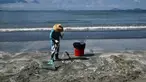 Seorang pria membersihkan sisa tumpahan minyak sawit dari pasir di sebuah pantai di Hong Kong, Senin (7/8). Sepuluh pantai di Hong Kong ditutup pada Minggu (6/8) setelah minyak sawit tumpah akibat tabrakan kapal di perairan China. (Anthony WALLACE / AFP)