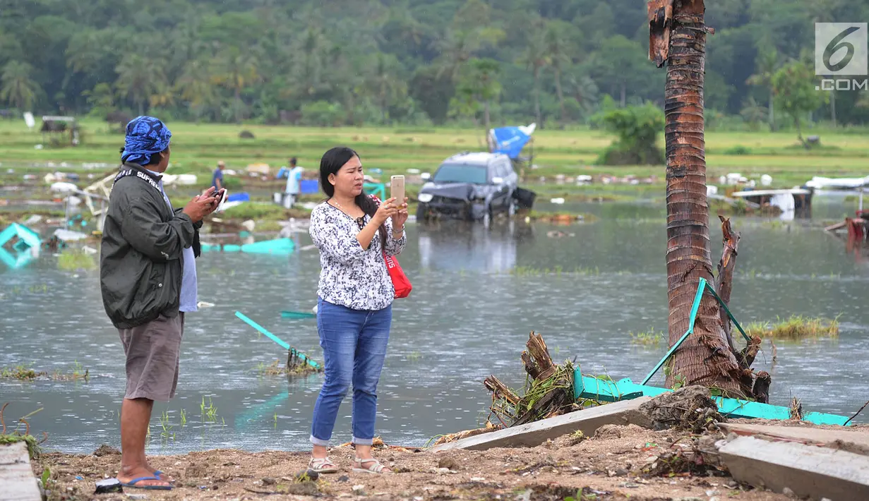 Warga berselfie dengan latar belakang kawasan terdampak bencana tsunami di Carita, Banten, Selasa (25/12). Libur Natal dimanfaatkan warga luar Anyer dan carita untuk menyaksikan langsung terdampak bencana sambil berselfie. (Merdeka.com/Arie Basuki)