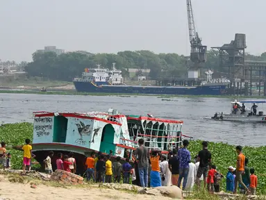 Orang-orang menyaksikan petugas pemadam kebakaran mencari korban kecelakaan feri di Sungai Shitalakshya di Narayanganj, Bangladesh (21/3/2022). Setidaknya enam mayat ditemukan dan 20 orang masih hilang setelah sebuah feri terbalik di sungai Shitalakkhya. (AFP/Munir uz Zaman)
