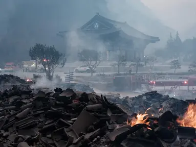 Bara api masih terlihat di antara puing-puing setelah sebagian besar bangunan hangus terbakar dalam kebakaran hutan di Kuil Gounsa, Uiseong, Korea Selatan pada 26 Maret 2025. (YASUYOSHI CHIBA/AFP)