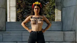 Aktivis perempuan Femen berdiri sambil menunjukkan tulisan "Illegitimate flag" di dadanya dan bendera Spanyol 'Celebrated violence bloody flag' saat unjuk rasa di monumen Konstitusi Spanyol 1978 di Madrid, (11/10). (AFP Photo/Oscar Del Pozo)