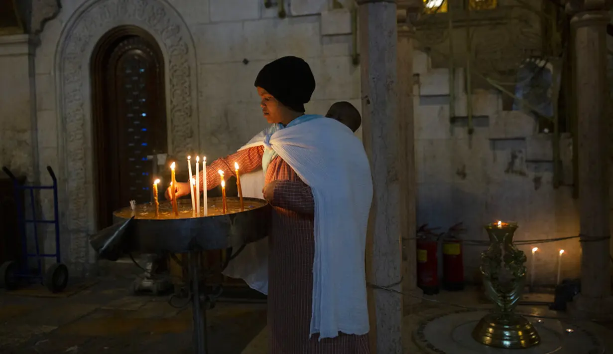 Seorang wanita menyalakan lilin dengan bayinya di punggung saat misa Kamis Putih di Kota Tua Yerusalem, Kamis (1/4/2021). Kamis Putih adalah hari Kamis sebelum Paskah dimana umat Kristen memiliki tradisi memperingati Perjamuan Malam terakhir yang dipimpin Yesus. (AP Photo/Maya Alleruzzo)