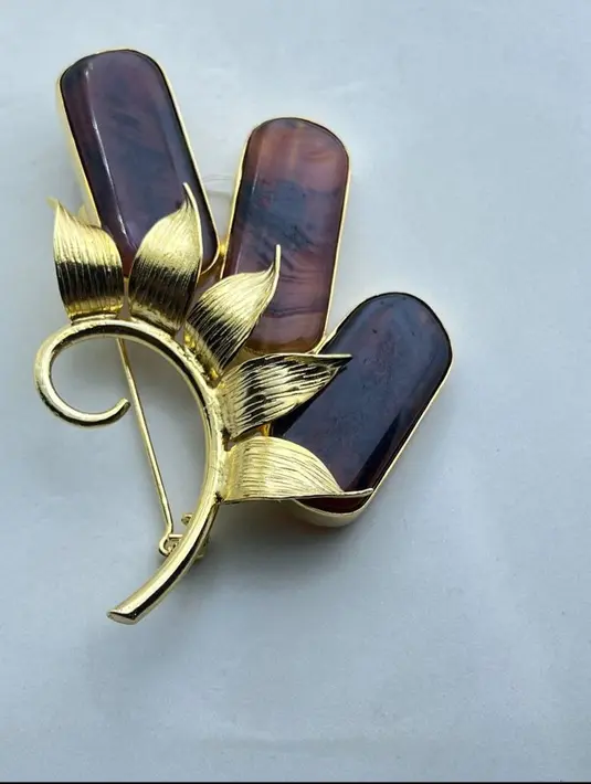 Bros elegan dengan desain floral ini memadukan kilau emas pada detail daun dengan tiga batu alam khas Kalimantan bernuansa cokelat kemerahan yang unik. Perpaduan material berkualitas dan desain artistik menjadikannya aksesori sempurna untuk mempercantik busana, baik untuk acara formal maupun kasual.[Dok/batualamkalimantan]