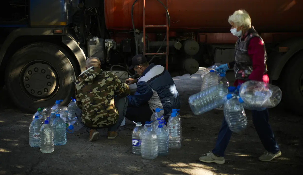 Pekerja mengisi ulang botol plastik dengan air di tempat penampungan untuk orang-orang yang terluka dan tunawisma di Izium, Ukraina, Rabu, 12 Oktober 2022. Dengan musim dingin yang semakin dekat, ada kekhawatiran serius tentang bagaimana orang akan bertahan hidup di suhu di bawah nol derajat tanpa panas. (AP Photo/Francisco Seco)