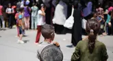 Anak-anak Palestina menyaksikan orang-orang mengantre untuk mendapatkan makanan hangat yang dibagikan oleh dapur amal di kamp pengungsi Nuseirat, Jalur Gaza tengah pada 15 Juli 2025. (Eyad BABA/AFP)