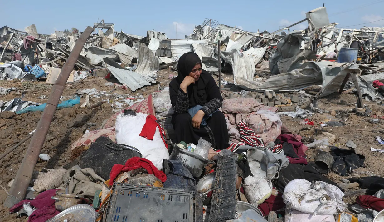 Seorang wanita Palestina yang terpaksa mengungsi duduk bersama barang-barangnya setelah serangan Israel di kamp pengungsi Deir el-Balah, Jalur Gaza tengah, pada 21 Agustus 2025. (Eyad BABA/AFP)