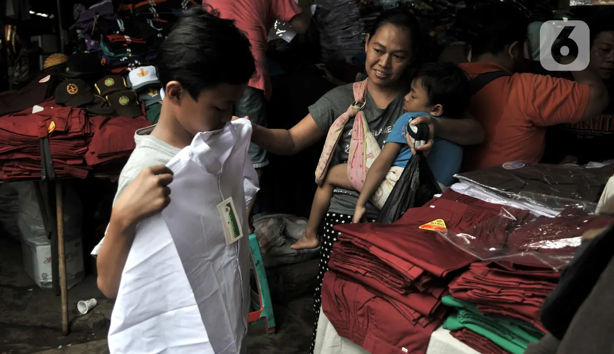 Pembeli mencoba seragam sekolah di Pasar Jatinegara, Jakarta, Minggu (5/1/2020). Jelang hari pertama belajar di semester baru, warga terdampak banjir di Kampung Melayu dan sekitarnya terpaksa membeli seragam baru untuk anaknya akibat banjir yang merendam rumah mereka. (merdeka.com/Iqbal Nugroho)