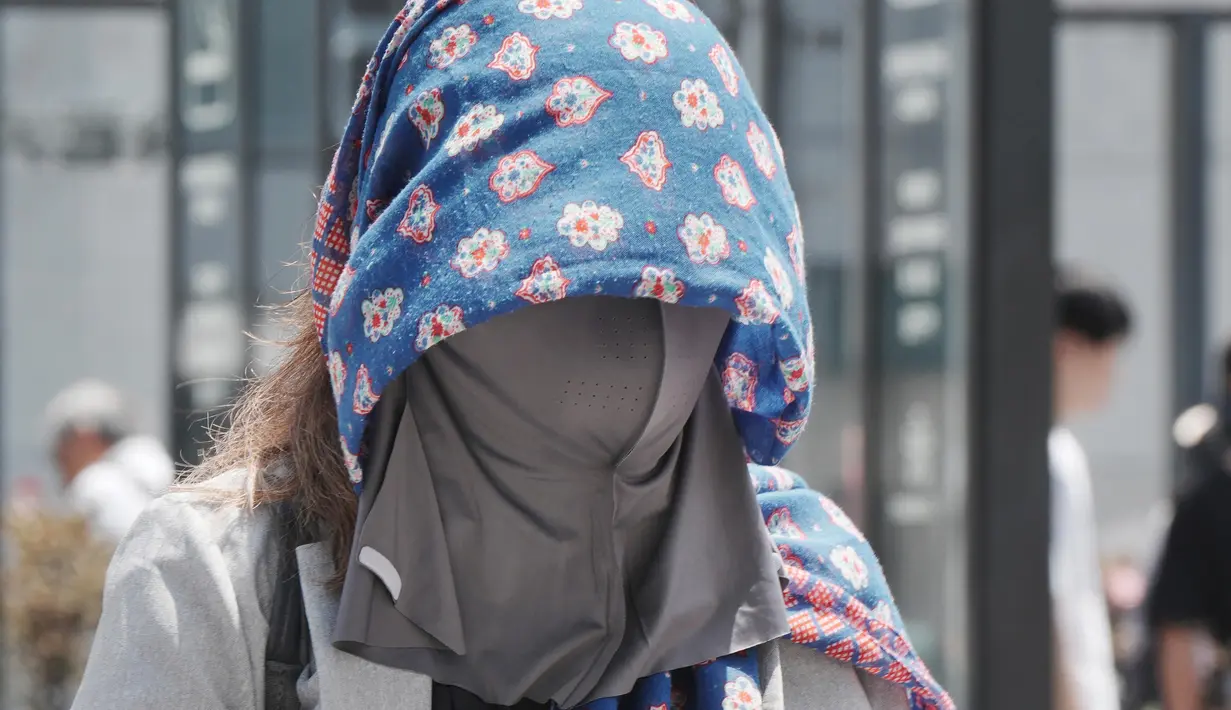 Seorang pejalan kaki mengenakan kain di atas kepalanya untuk melindungi diri dari panas dan terik matahari di Tokyo pada 5 Agustus 2025. (Kazuhiro NOGI/AFP)