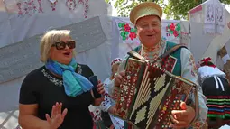 Seorang wanita berfoto dengan musisi yang mengenakan kostum tradisional di Minsk, Belarus, 26 September 2020. Berbagai pameran pertanian digelar di seluruh Belarus untuk merayakan panen musim gugur. (Xinhua/Henadz Zhinkov)