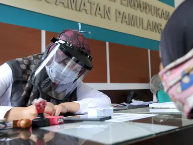 Petugas Dinas Kependudukan dan Catatan Sipil menggunakan pelindung wajah saat melayani warga di Kecamatan Pamulang, Tangerang Selatan, Rabu (3/6/2020). Sejumlah kantor pelayanan pemerintah melaksanakan protokol kesehatan yang ketat untuk memutus rantai penyebaran covid-19. (merdeka.com/Arie Basuki)