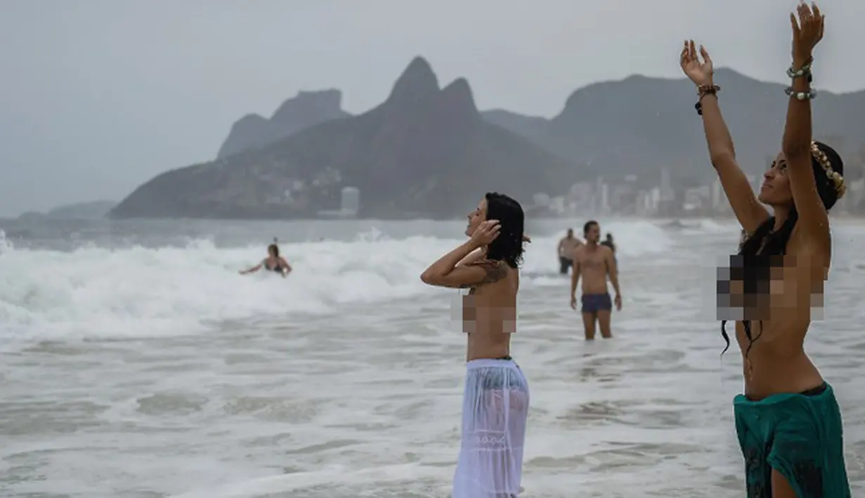 Tanpa riskan, kedua wanita ini asyik melakukan ritual Lemanja meski tak menutup dadanya, Pantai Arpoador, Rio de Janeiro, Brasil, Senin (2/2/2015). (AFP Photo/Yasuyoshi Chiba)