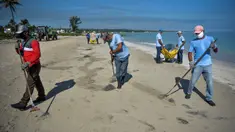 Para pekerja dengan mengenakan masker membersihkan pantai di Havana pada Senin (15/6/2020). Kuba akan menguji semua pelancong untuk Covid-19 dan membatasi kontak mereka dengan penduduk setempat ketika perbatasan dibuka kembali untuk turis asing. (Yamil LAGE / AFP)