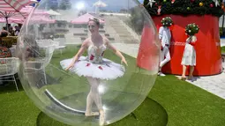 Seorang penari balet berpose dalam gelembung plastik raksasa saat menghibur warga yang berbelanja menjelang libur Natal di tengah pandemi Covid-19 di Melbourne, Australia pada 13 Desember 2020. (Photo by William WEST / AFP)