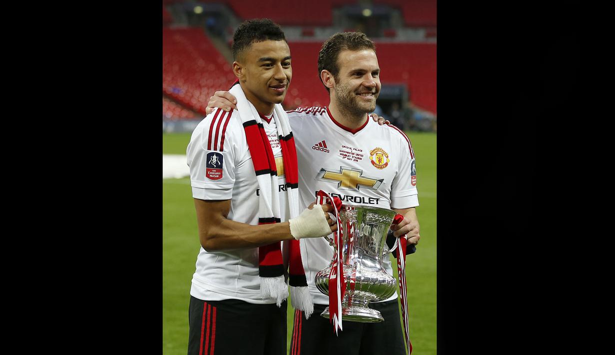 Pemain MU, Jesse Lingard (kiri) dan Juan Mata memegang trofi Piala FA setelah mengalahkan Crystal Palace dan keluar sebagai juara Piala FA 2015/2016. Kedua pemain tersebut menjadi pahlawan dengan mencetak masing-masing satu gol bagi kemenangan 2-1 Setan Merah atas Crystal Palace. (AFP/Ian Kington)