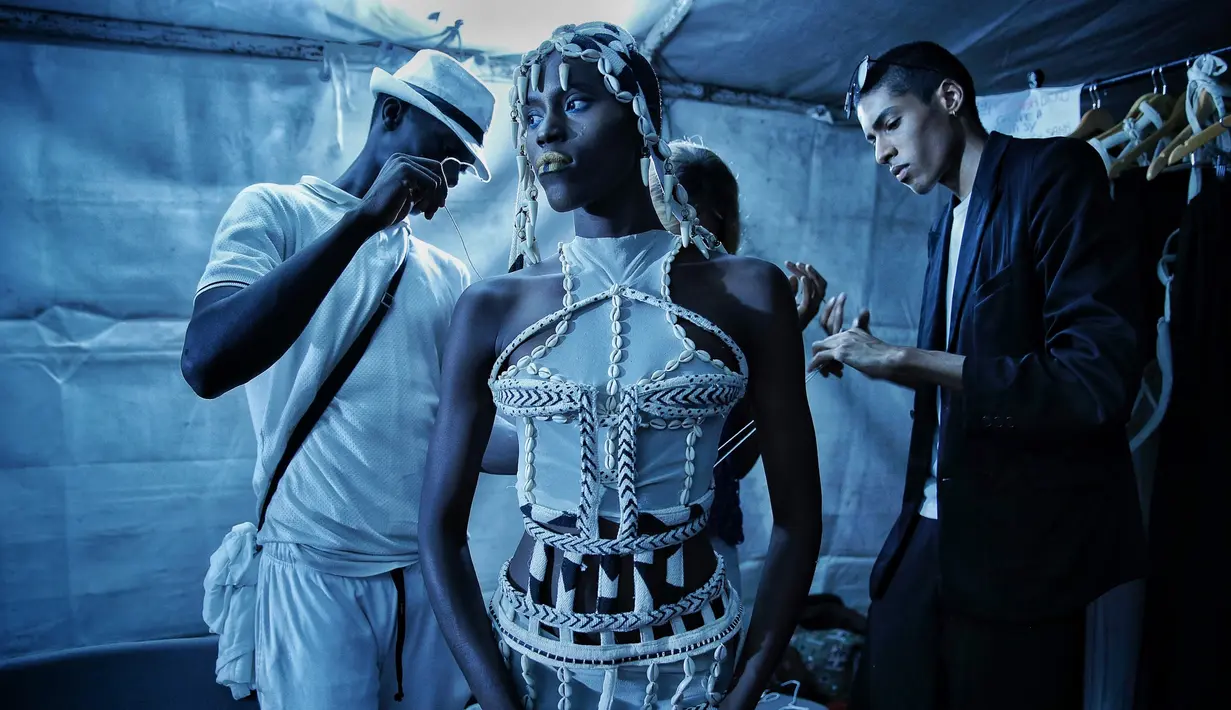 Desainer Oumar Dicko (kanan) dari Mali dan Belgia memakaikan busana kreasinya ke salah satu model  belakang panggung Dakar Fashion Week di ibukota Senegal, (1/7). (AP Photo / Finbarr O'Reilly)