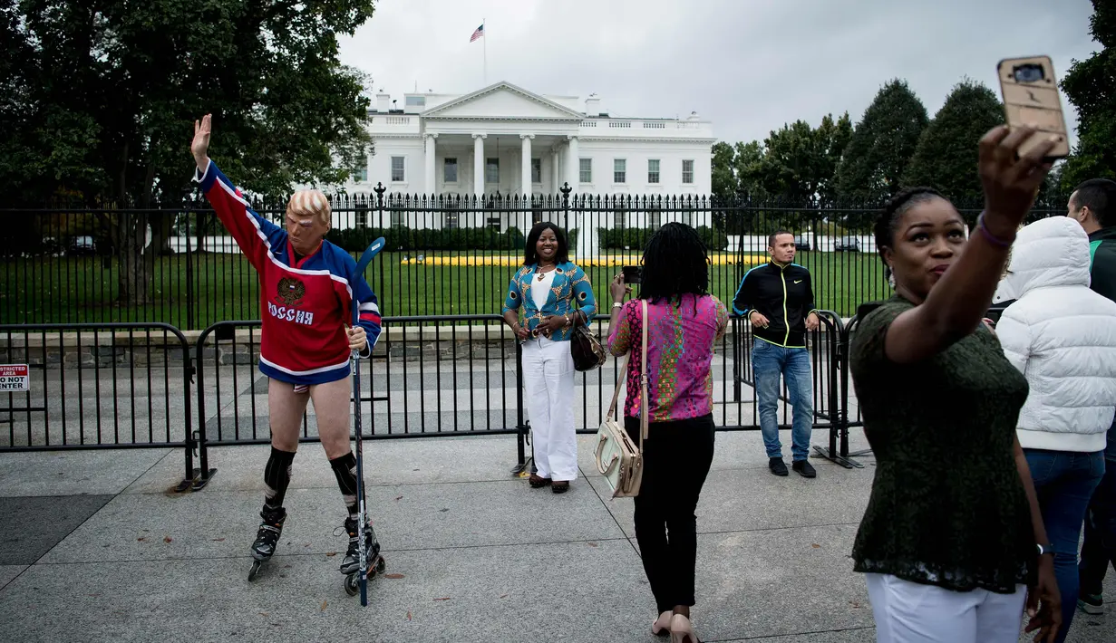 Wisatawan melihat seorang pria mengenakan topeng Presiden AS Donald Trump dan kostum tim hoki Rusia saat unjuk rasa di luar Gedung Putih di Pennsylvania Avenue di Washington, DC, (29/10). (AFP Photo/Brendan Smialowski)