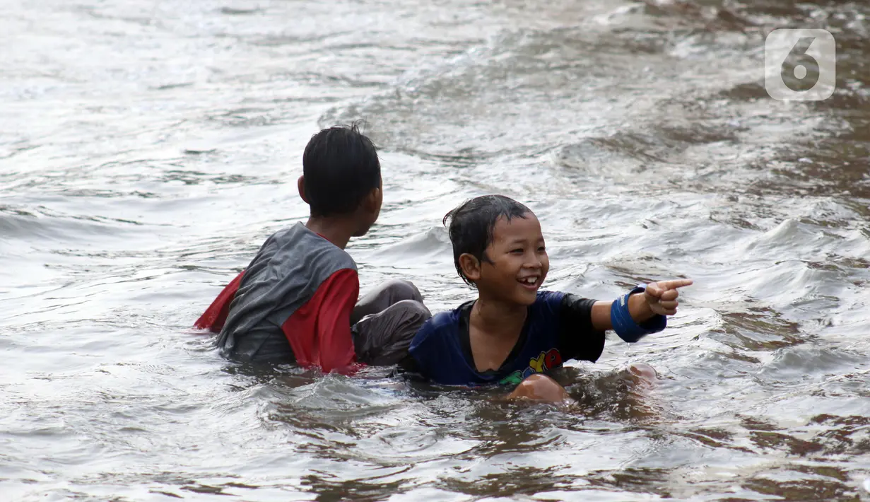Anak-anak bermain di genangan air akibat banjir rob di kawasan pintu masuk Pelabuhan Nizam Zachman, Muara Baru, Jakarta, Jumat (5/6/2020). Banjir rob di Pelabuhan Muara Baru tersebut terjadi akibat cuaca ekstrem serta pasang air laut. (Liputan6.com/Helmi Fithriansyah)