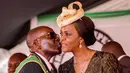 Presiden Zimbabwe, Robert Mugabe mencium istrinya Grace Mugabe saat perayaan Hari Kemerdekaan ke-37 negaranya di Stadion Olahraga Nasional di Harare (18/3). Polisi telah menyelidiki dugaan serangan Grace Mugabe. (AFP Photo/Jekesai Njikizana)