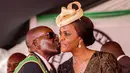 Presiden Zimbabwe, Robert Mugabe mencium istrinya Grace Mugabe saat perayaan Hari Kemerdekaan ke-37 negaranya di Stadion Olahraga Nasional di Harare (18/3). Polisi telah menyelidiki dugaan serangan Grace Mugabe. (AFP Photo/Jekesai Njikizana)