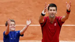 Petenis Serbia, Novak Djokovic, merayakan kemenangannya atas petenis Spanyol, Roberto Bautista Agut, bersama seorang ball boy dalam turamen tenis Prancis Terbuka 2016 di Roland Garros, Paris, (1/6/2016). (Reuters/Pascal Rossignol)