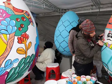 Para pelukis menghias telur-telur besar menjelang perayaan tahun baru Nowruz di Taman Mellat, Teheran, pada 27 Februari 2024. (ATTA KENARE/AFP)